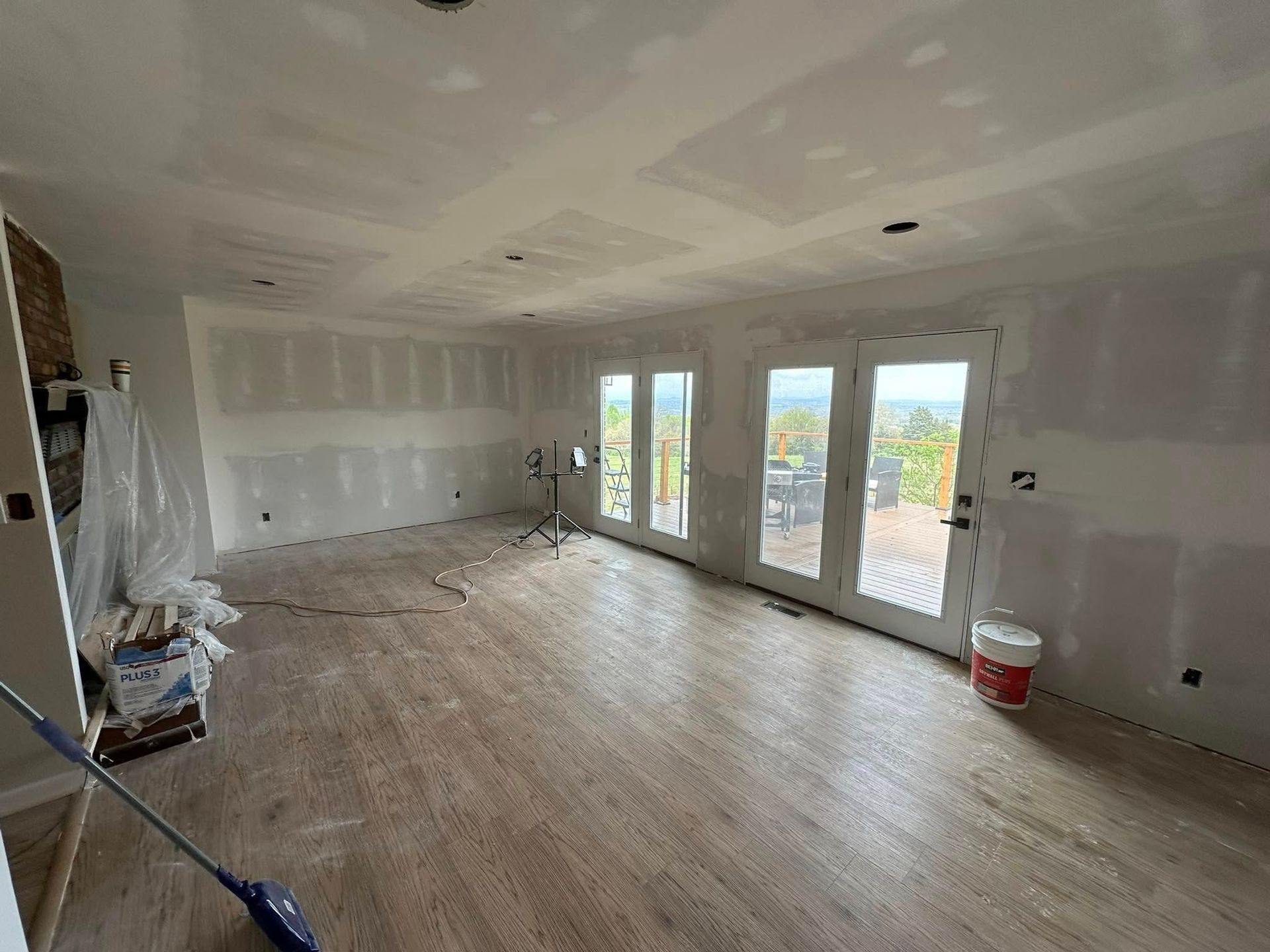 Empty unfinished room with drywall, hardwood floors, and large glass doors opening to a deck.
