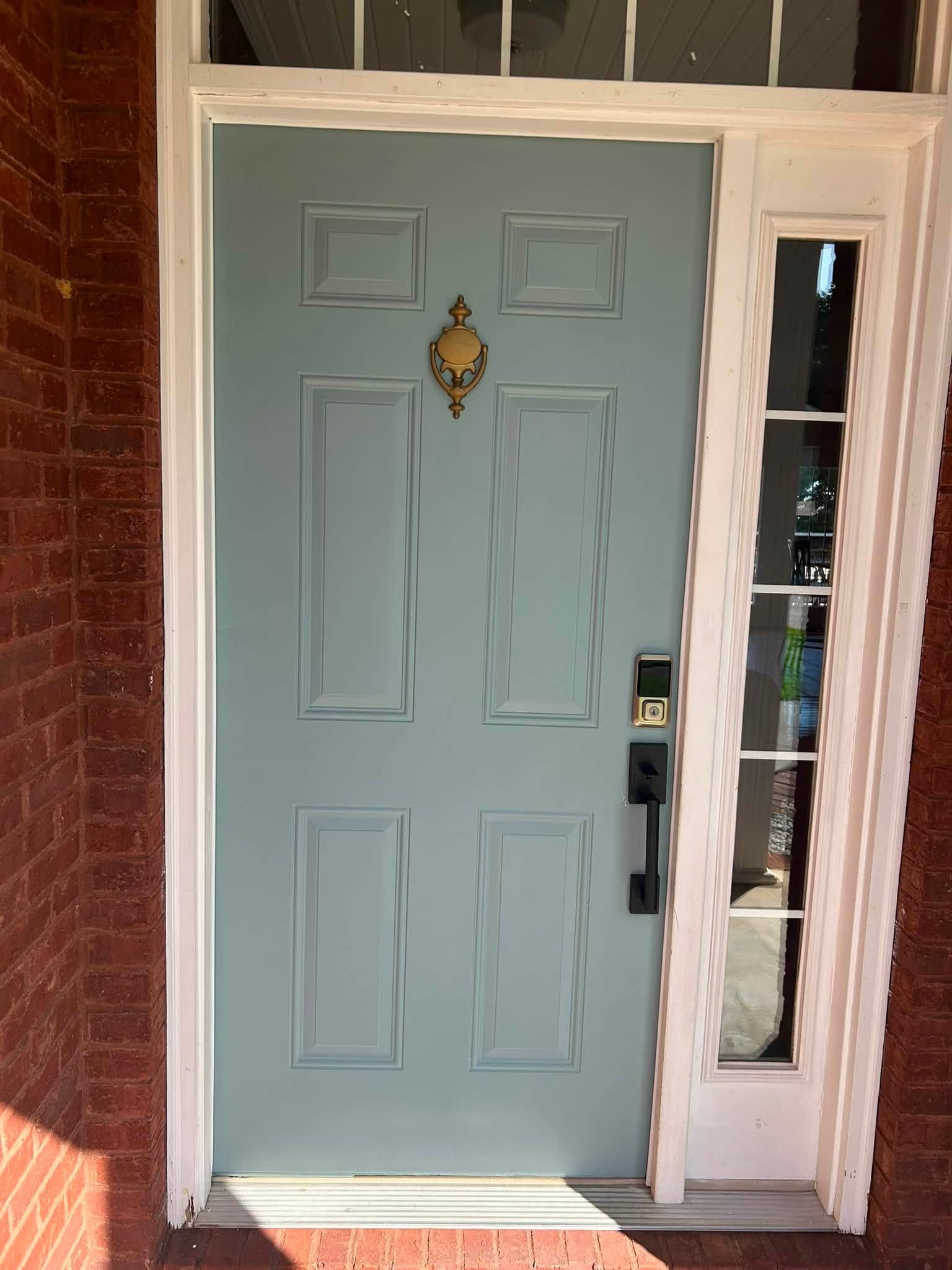 Light blue front door beside a narrow glass sidelight, set in a brick entryway.