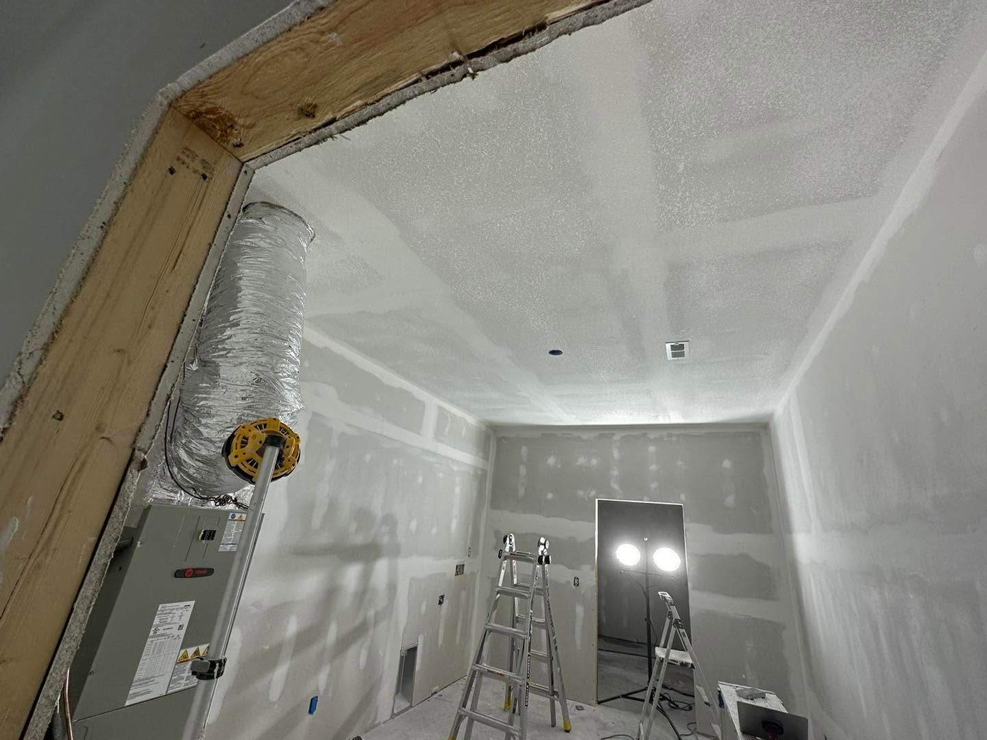 Unfinished drywall room under construction with ladder, electrical panel, and doorway openings.
