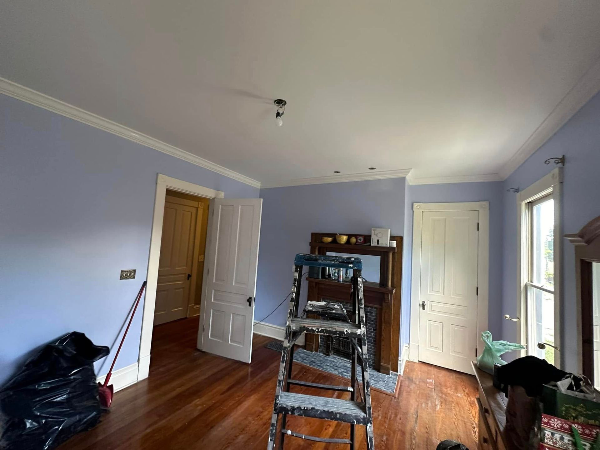 Blue-walled room with hardwood floors, a ladder in the center, and doors and windows along the walls.