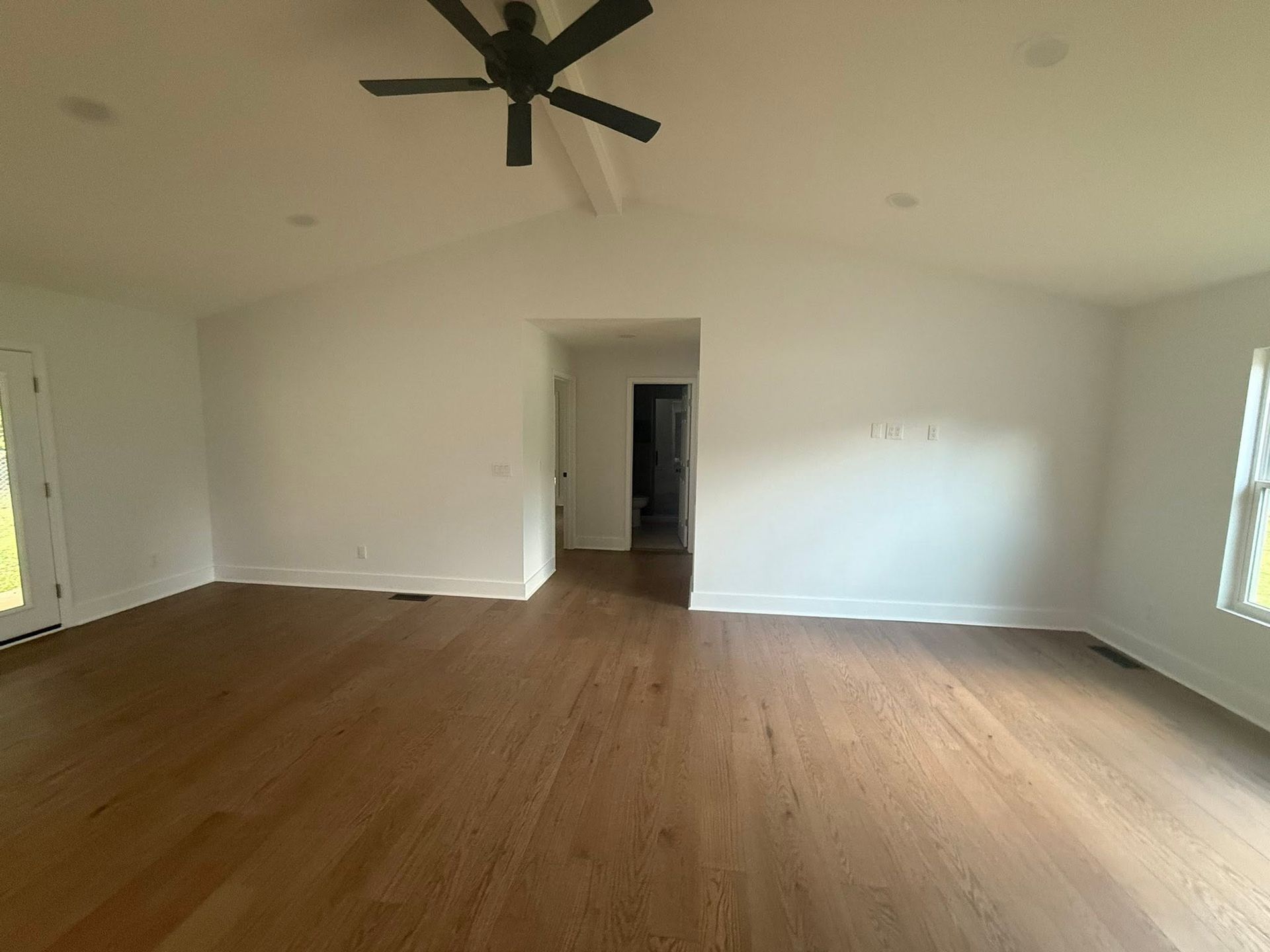 Empty living room with hardwood floors, white walls, ceiling fan, and windows on both sides.
