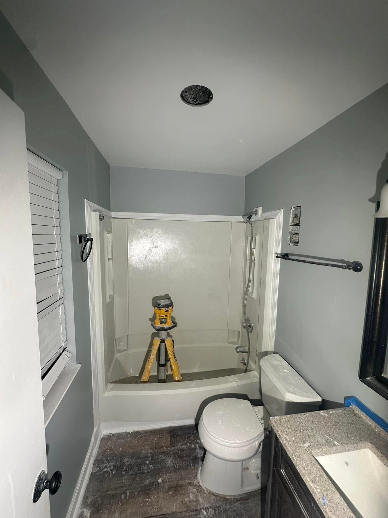 Small bathroom with an open shower, toilet, sink, and a yellow tripod in the shower area.