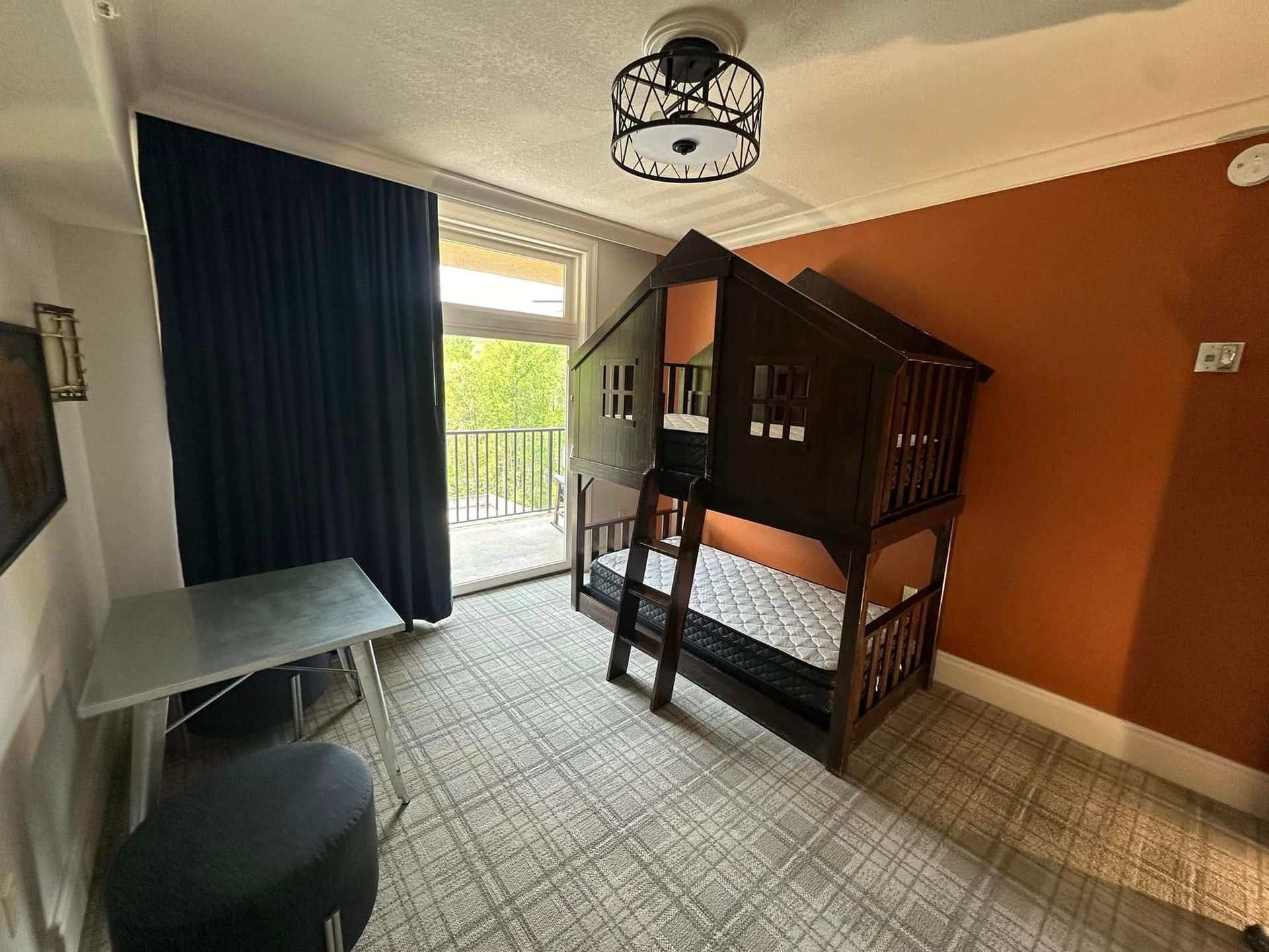 Small bedroom with a bunk bed, desk, dark curtains, and balcony door leading outside.