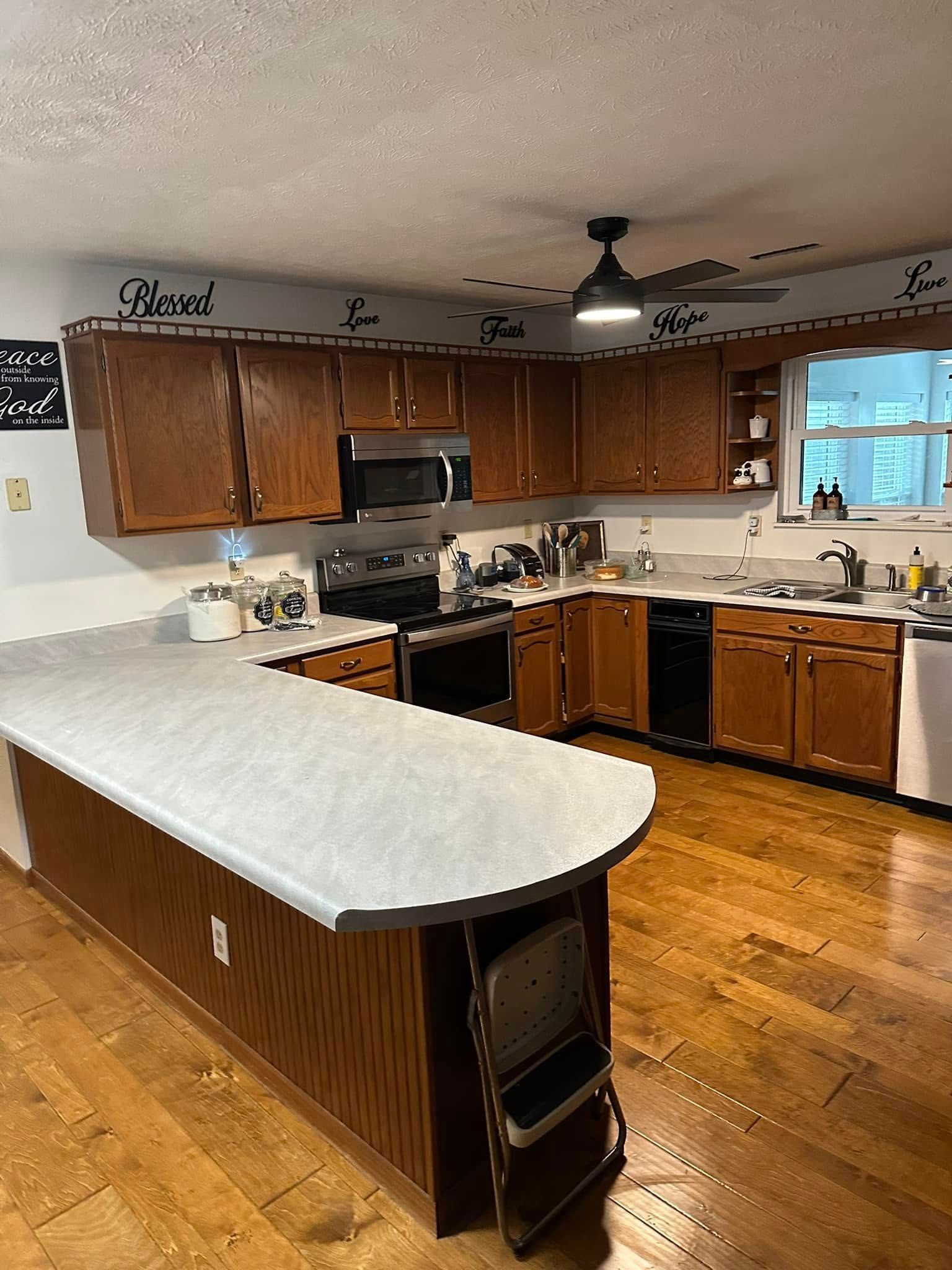 Kitchen with wooden cabinets, white island countertop, stainless appliances, and hardwood floors.