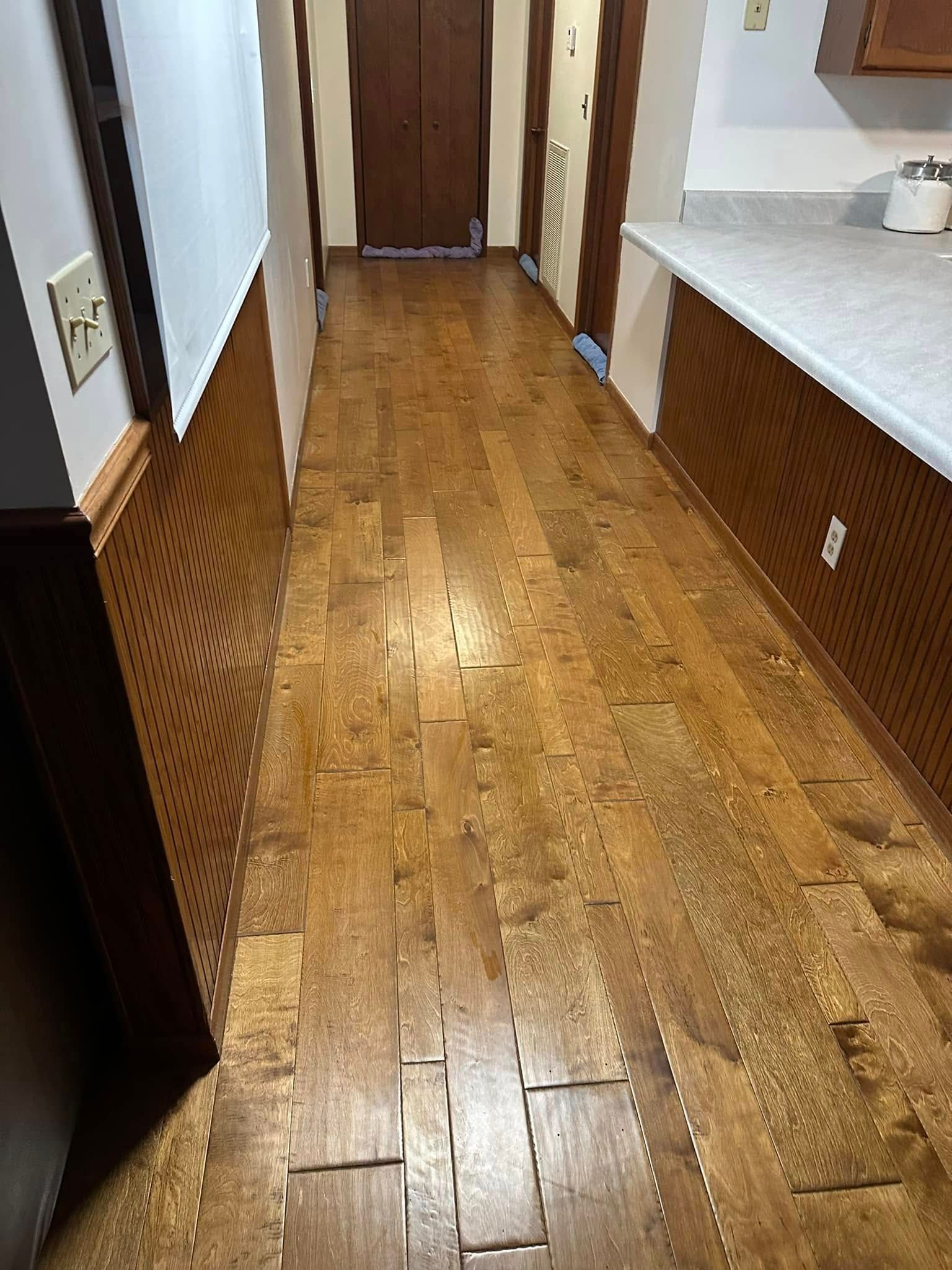 Narrow hallway with hardwood floors, brown wood wainscoting, and a closed door at the end