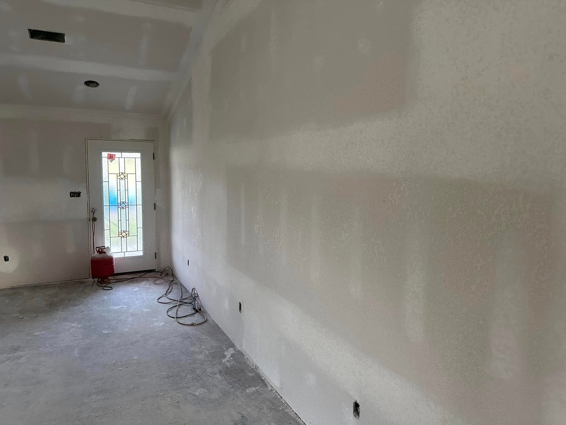 Empty white room under construction with unfinished walls, floor, and a glass door at the end.