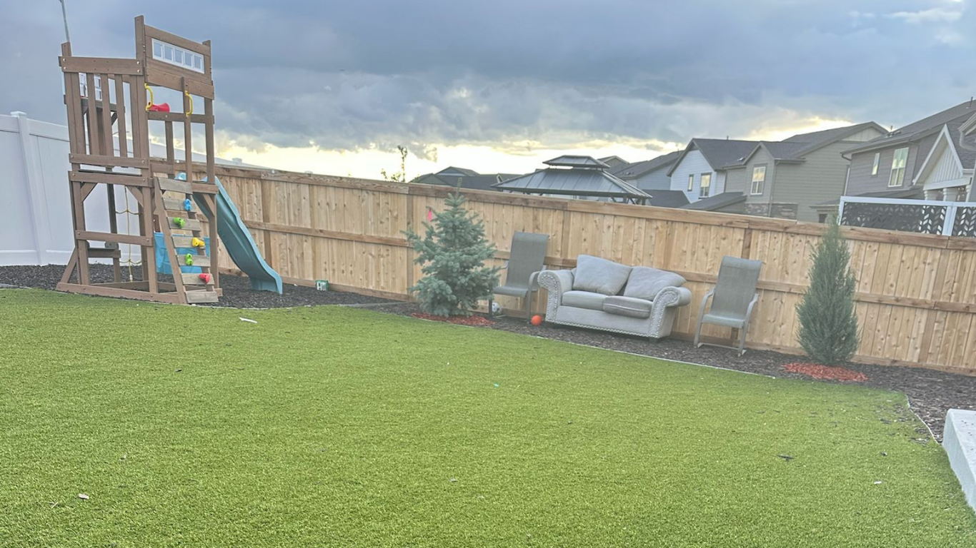 Backyard with playset, couch, chairs, and bamboo fence. Overcast sky.