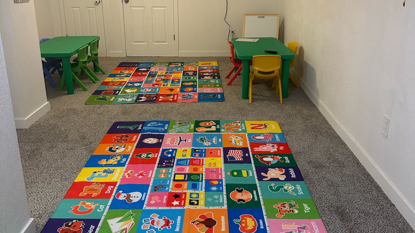 Child-sized classroom with colorful alphabet rug, two small tables, and green/yellow chairs