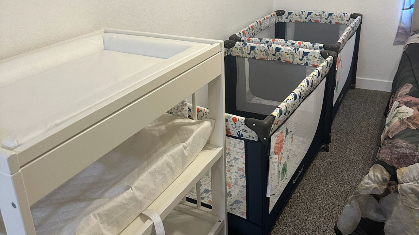 White changing table with shelf, and two blue playards in a room.