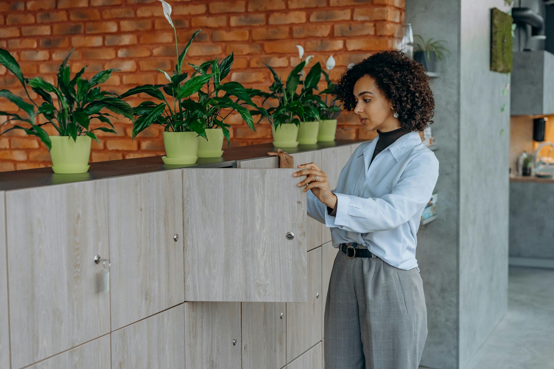 Person using a smartphone beside potted plants on a wooden cabinet in a modern office hallway