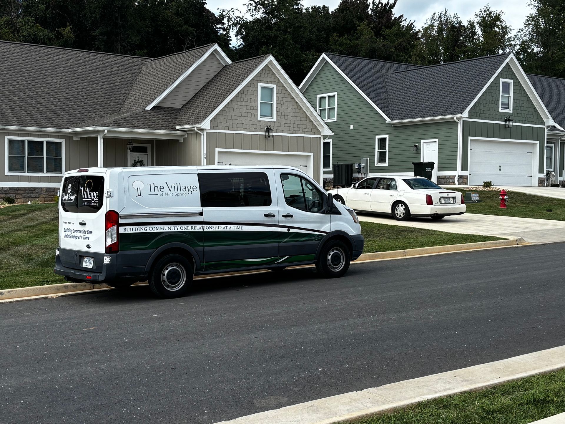 A white and green van parked on a street in front of newly built houses.