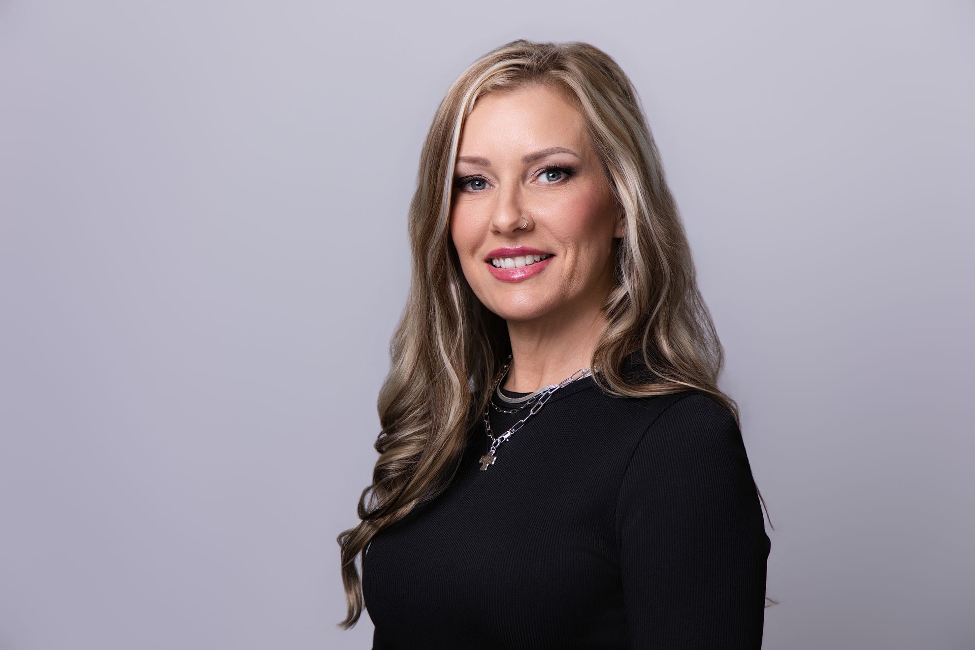 Portrait of a smiling woman with long blonde hair in a black top against a light gray background