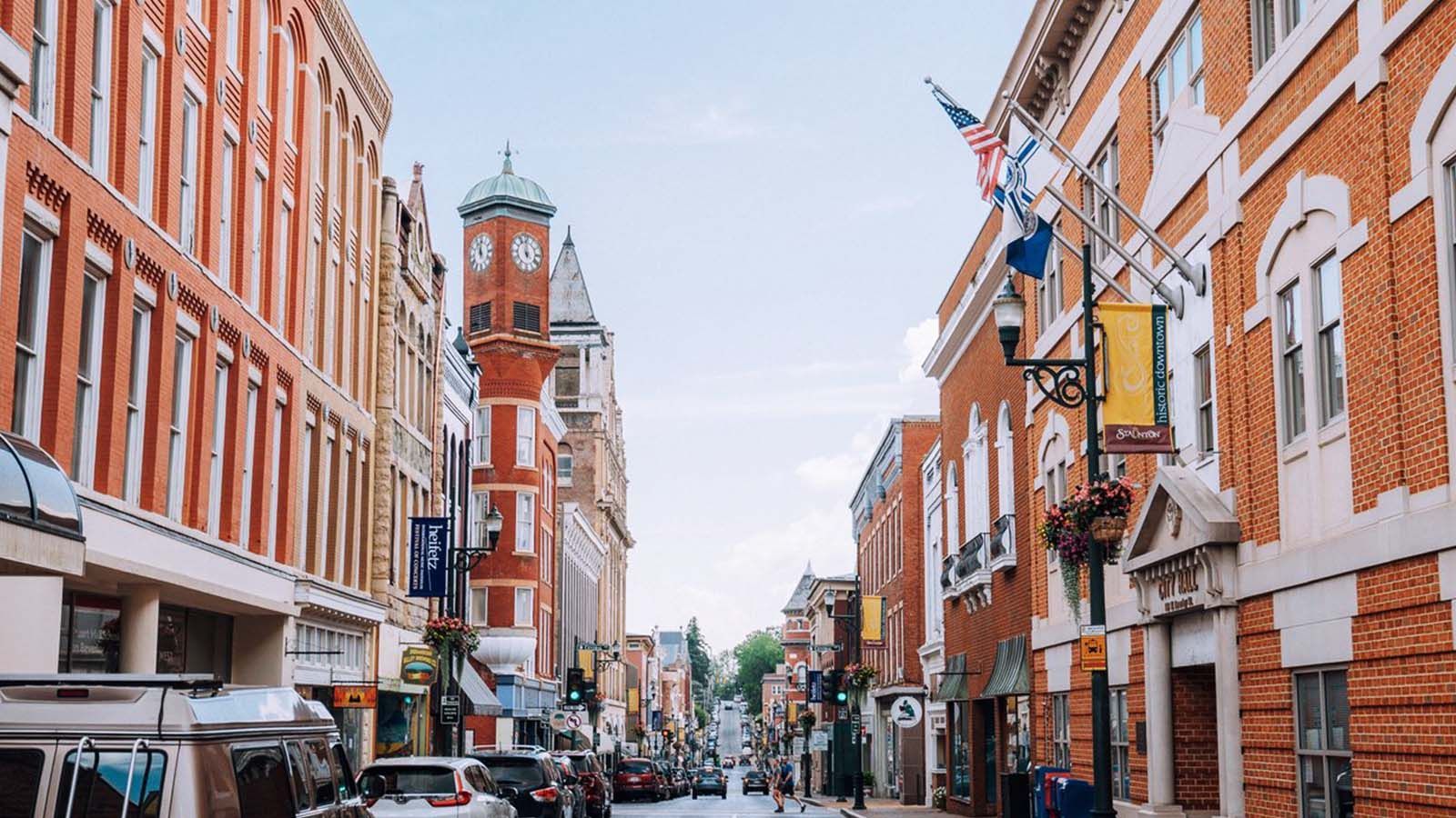 Street lined with brick buildings, clock tower in the distance, blue sky.