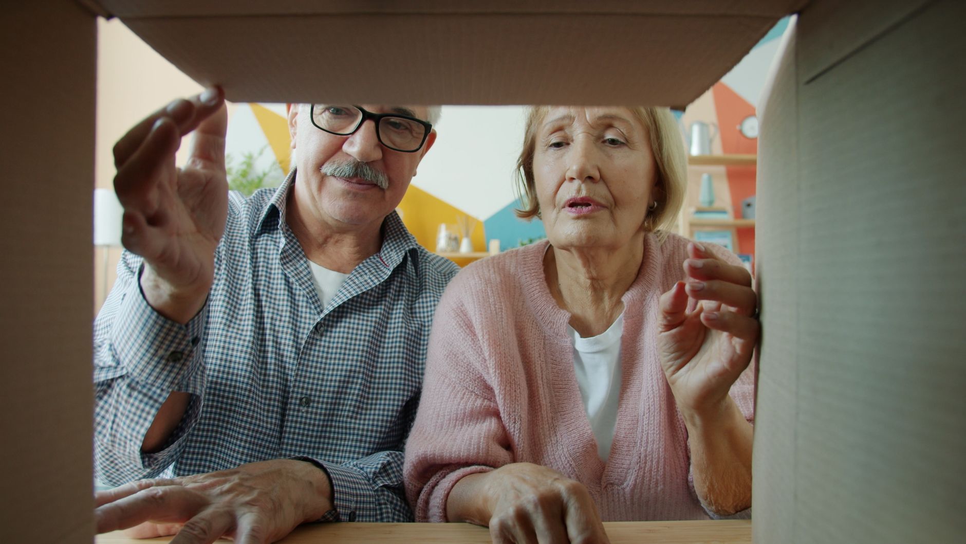 Older couple looking into an open moving box together in their living room