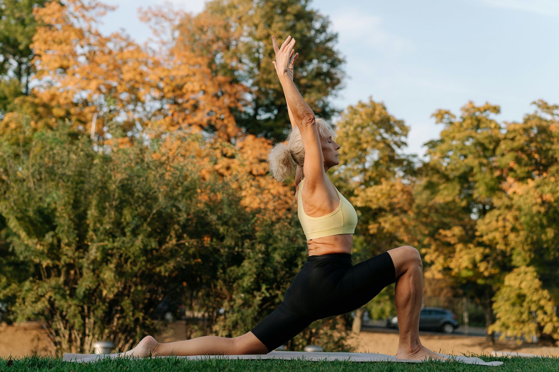 Woman in yoga pose outdoors with arms raised.