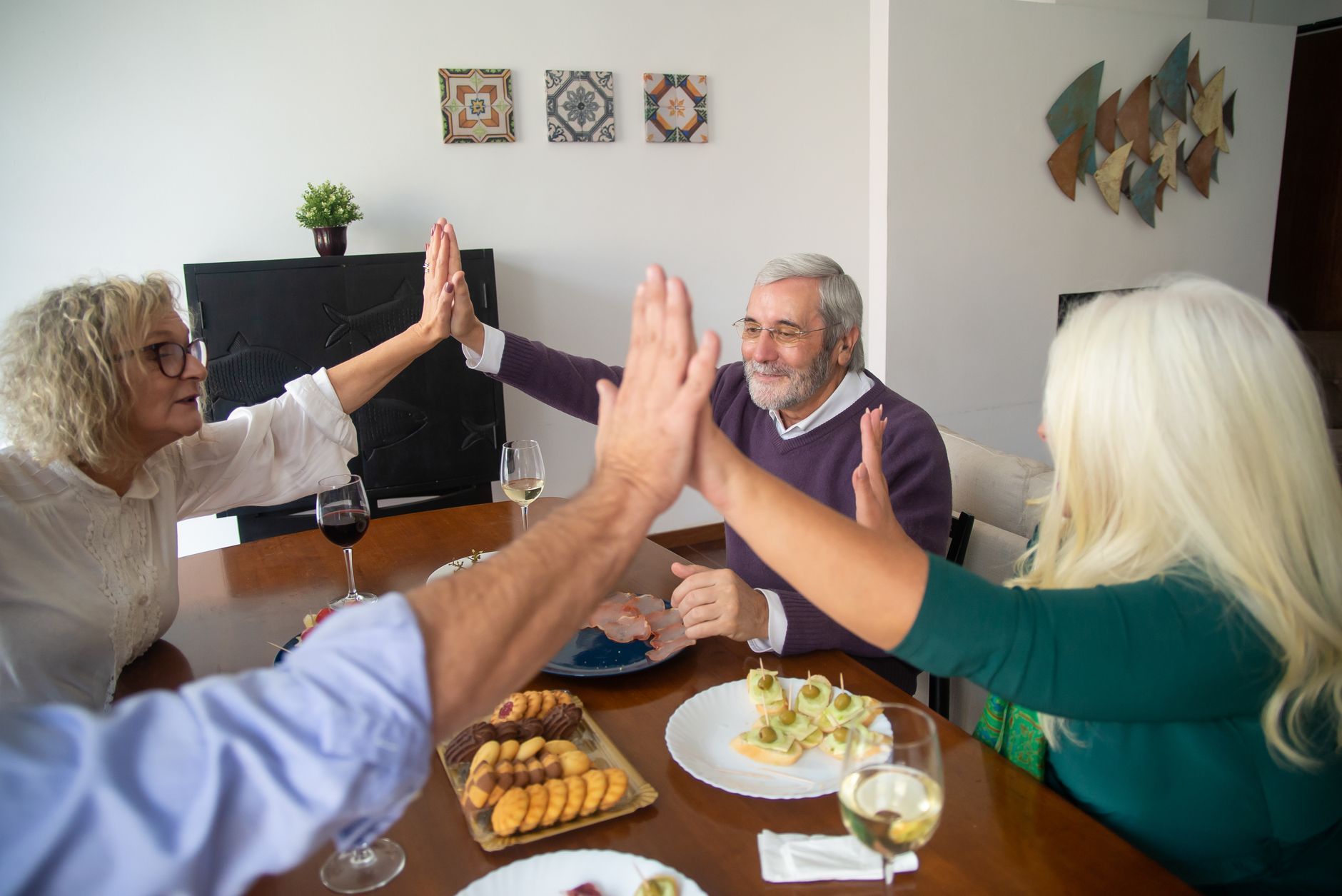 Older friends sharing a high five over snacks at a dinner table
