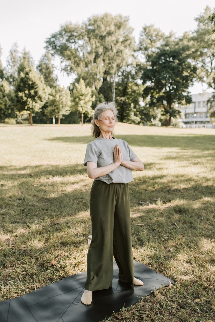 Older woman doing yoga on a mat in a sunny park