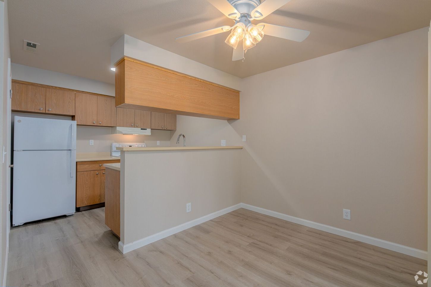 An empty apartment with a kitchen and a ceiling fan.