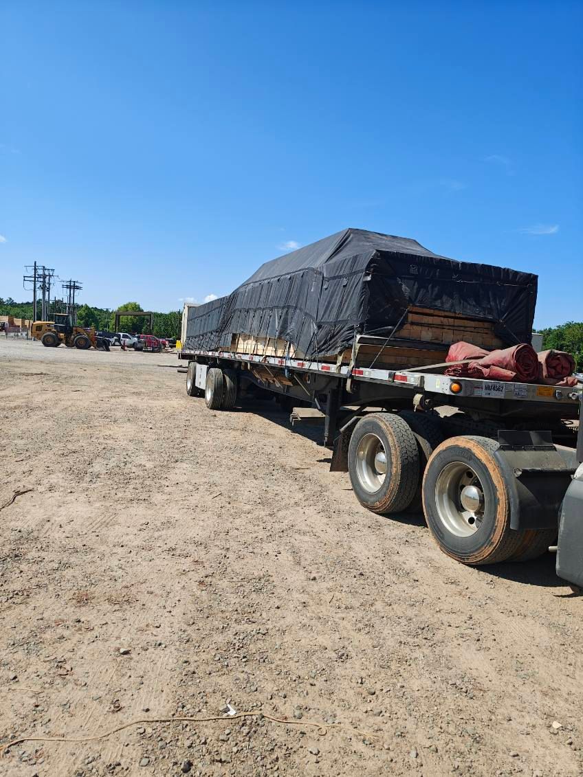 Cargo truck with covered load parked on a dusty lot under a clear blue sky.