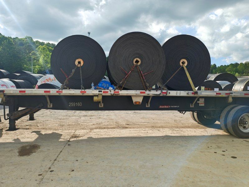Large black cable rolls strapped on a flatbed trailer in an outdoor yard.