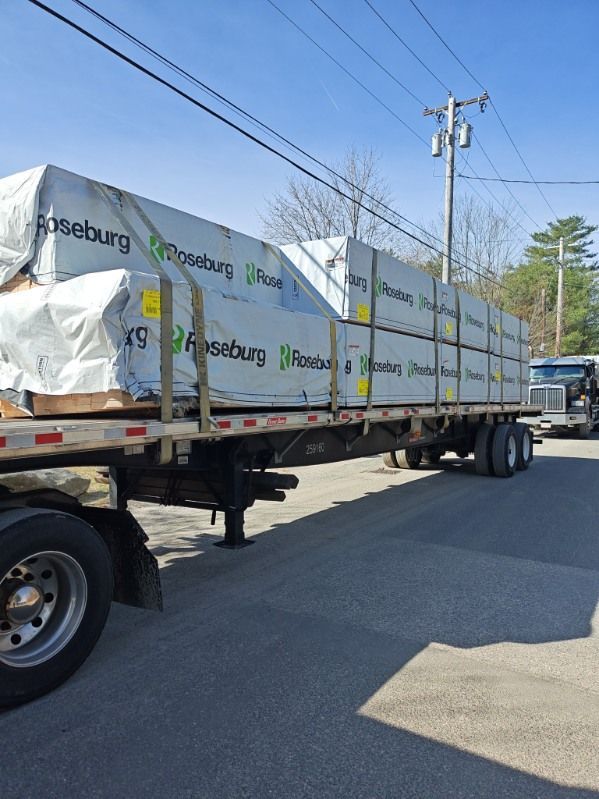 Flatbed truck carrying wrapped cargo on a sunny street with utility poles overhead