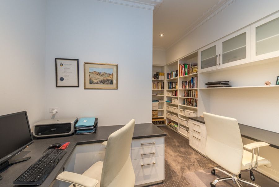 A home office with two desks , two chairs , a computer and a printer.