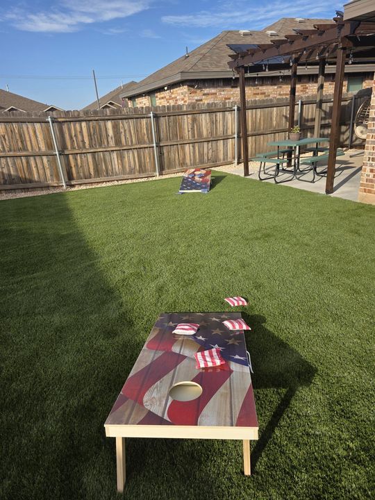 Backyard patio with a small table and chairs on a grassy lawn under a clear blue sky.
