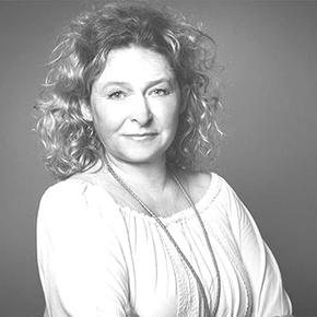 Frau mit lockigem Haar, lächelnd, trägt ein helles Oberteil und eine helle Halskette, Studioaufnahme.