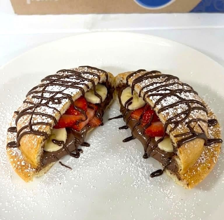 Chocolate-drizzled strawberry and banana crepes dusted with powdered sugar on a white plate