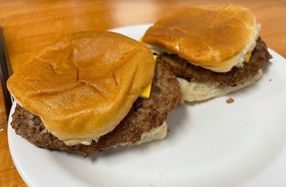 Two cheeseburgers on a white plate, with toasted buns and melted cheese