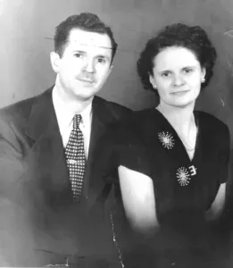 Black-and-white studio portrait of a seated couple in formal clothing, facing the camera.