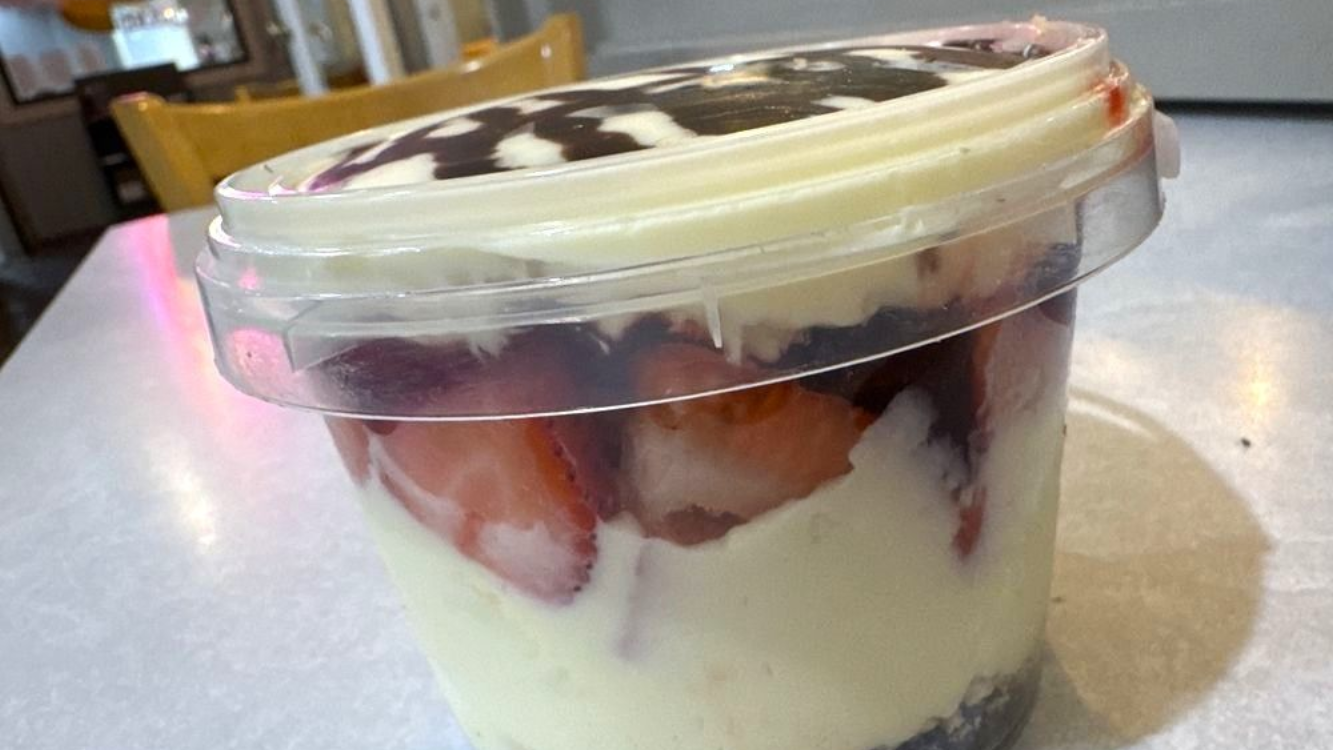 Clear plastic cup of layered dessert with cream and strawberries on a table