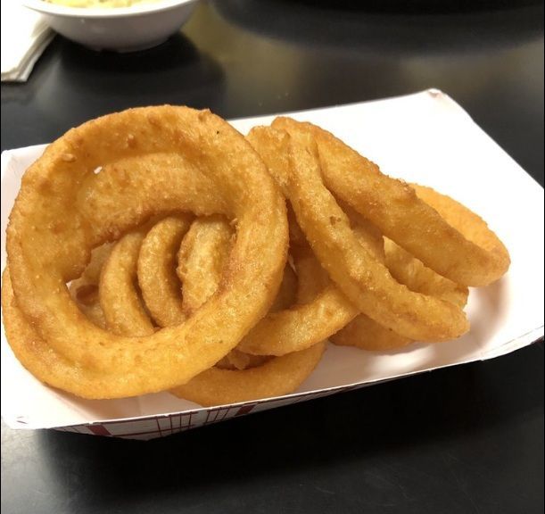 Golden onion rings stacked in a white paper tray on a dark table.