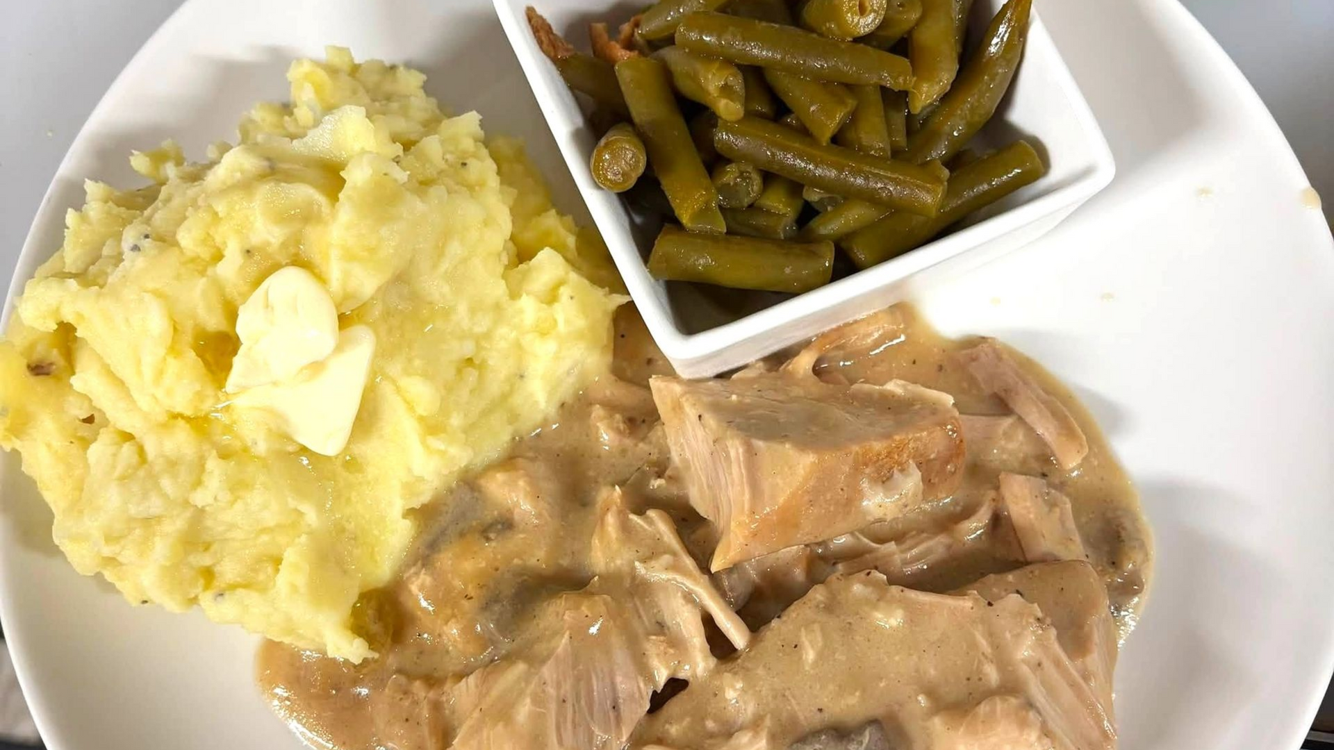 Mashed potatoes, green beans, and sliced meat on a white dinner plate