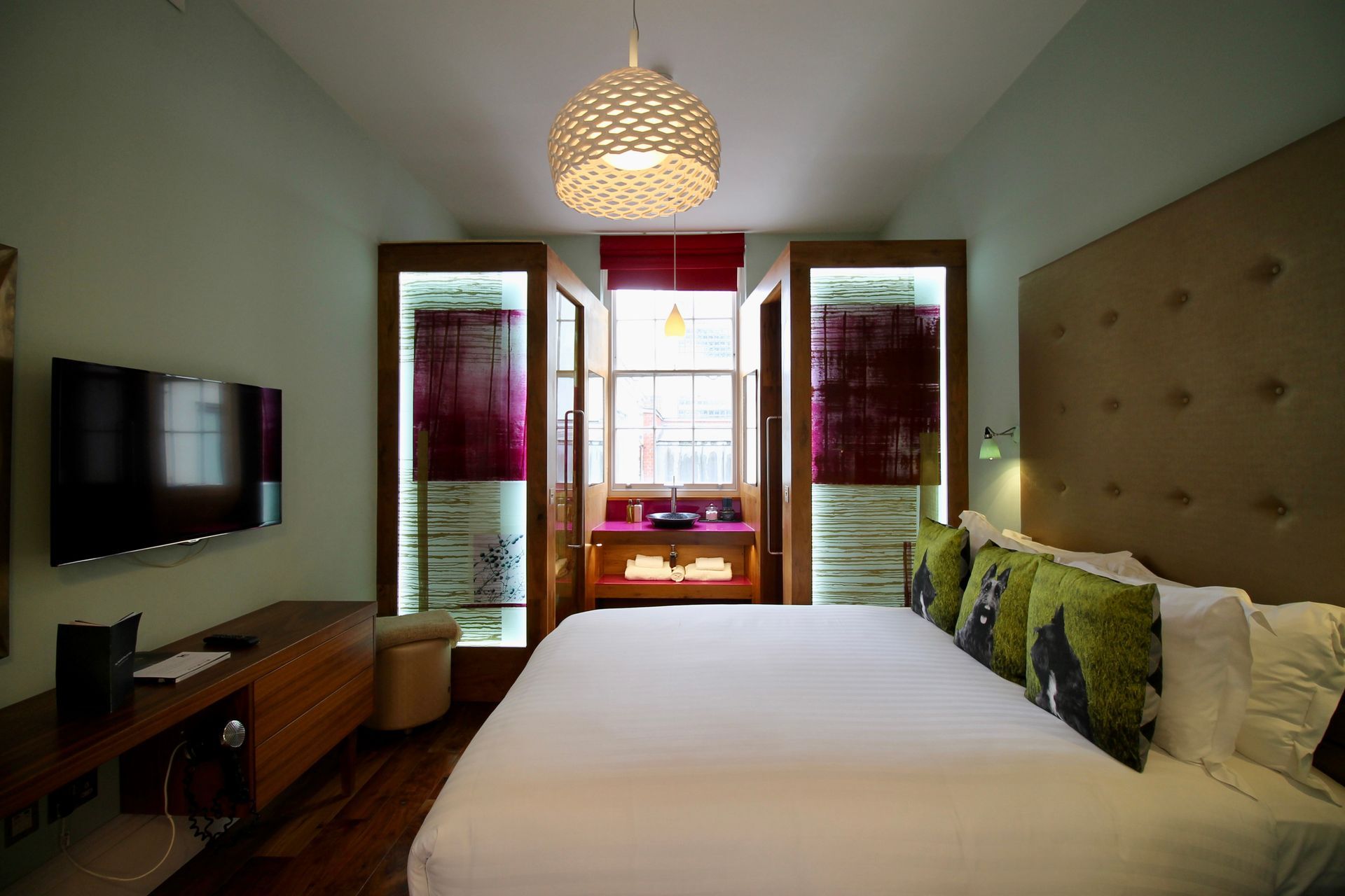 Modern bedroom with a bed, wall-mounted TV, and open balcony doors letting in natural light