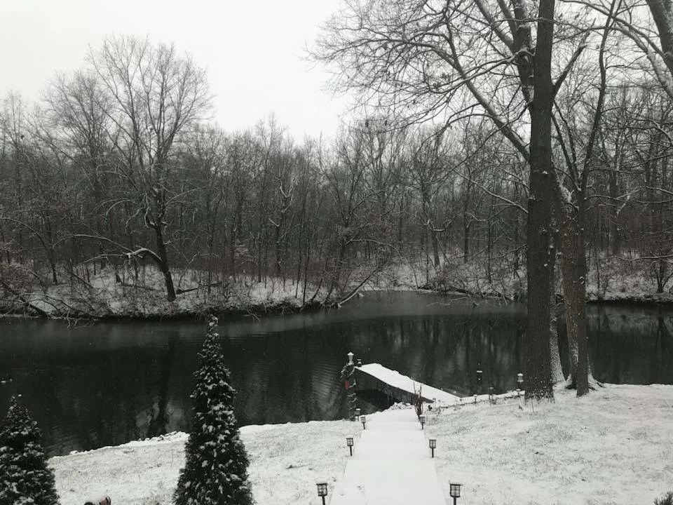 Snowy landscape with a river and a small dock. Bare trees line the water's edge.