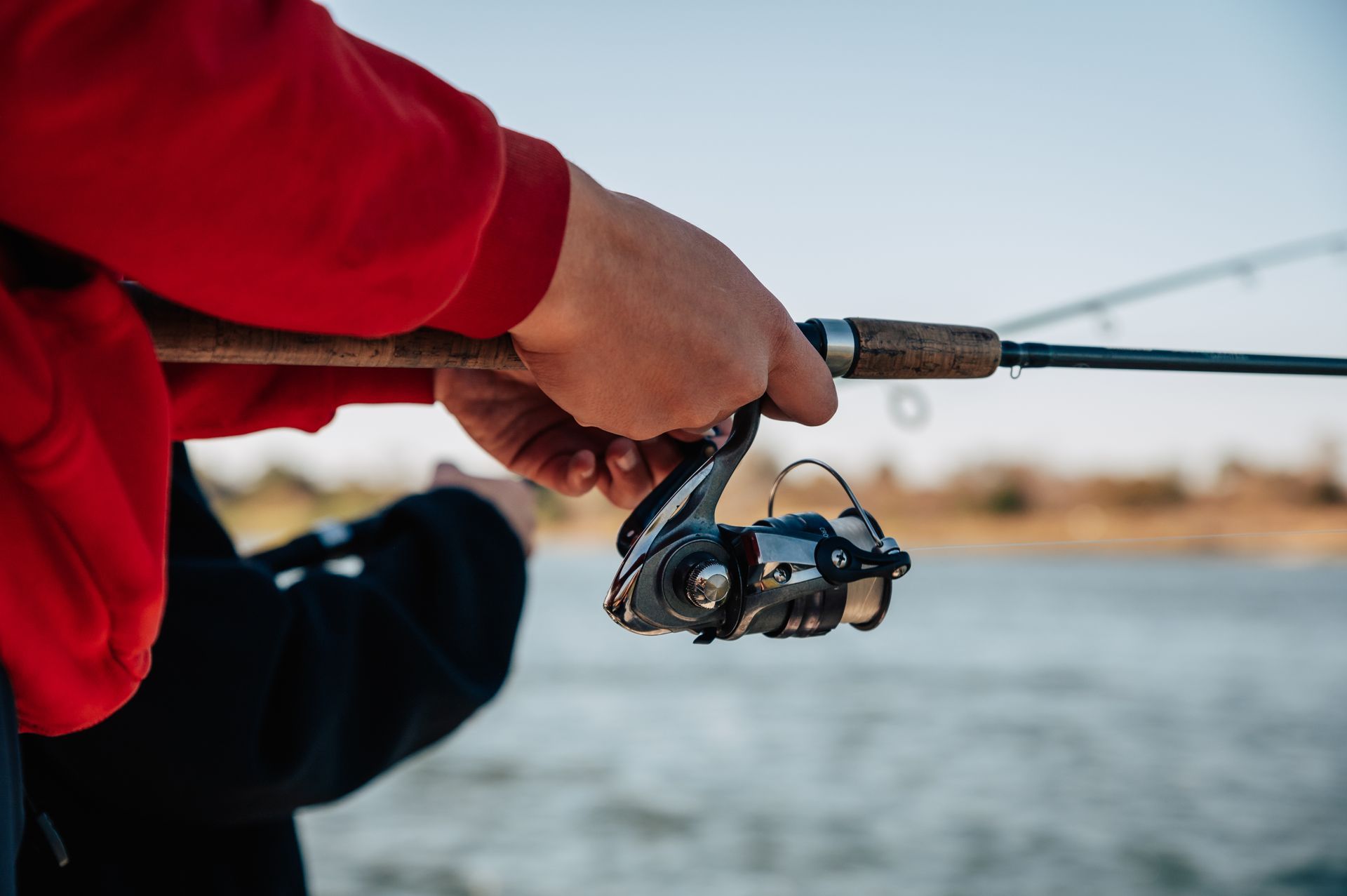Person in red sweater holds fishing rod over water.