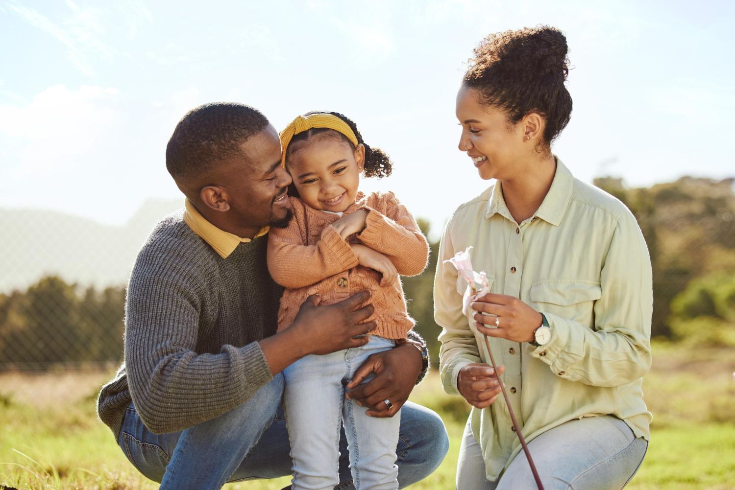 A man is kissing a little girl on the cheek while a woman holds a flower. 