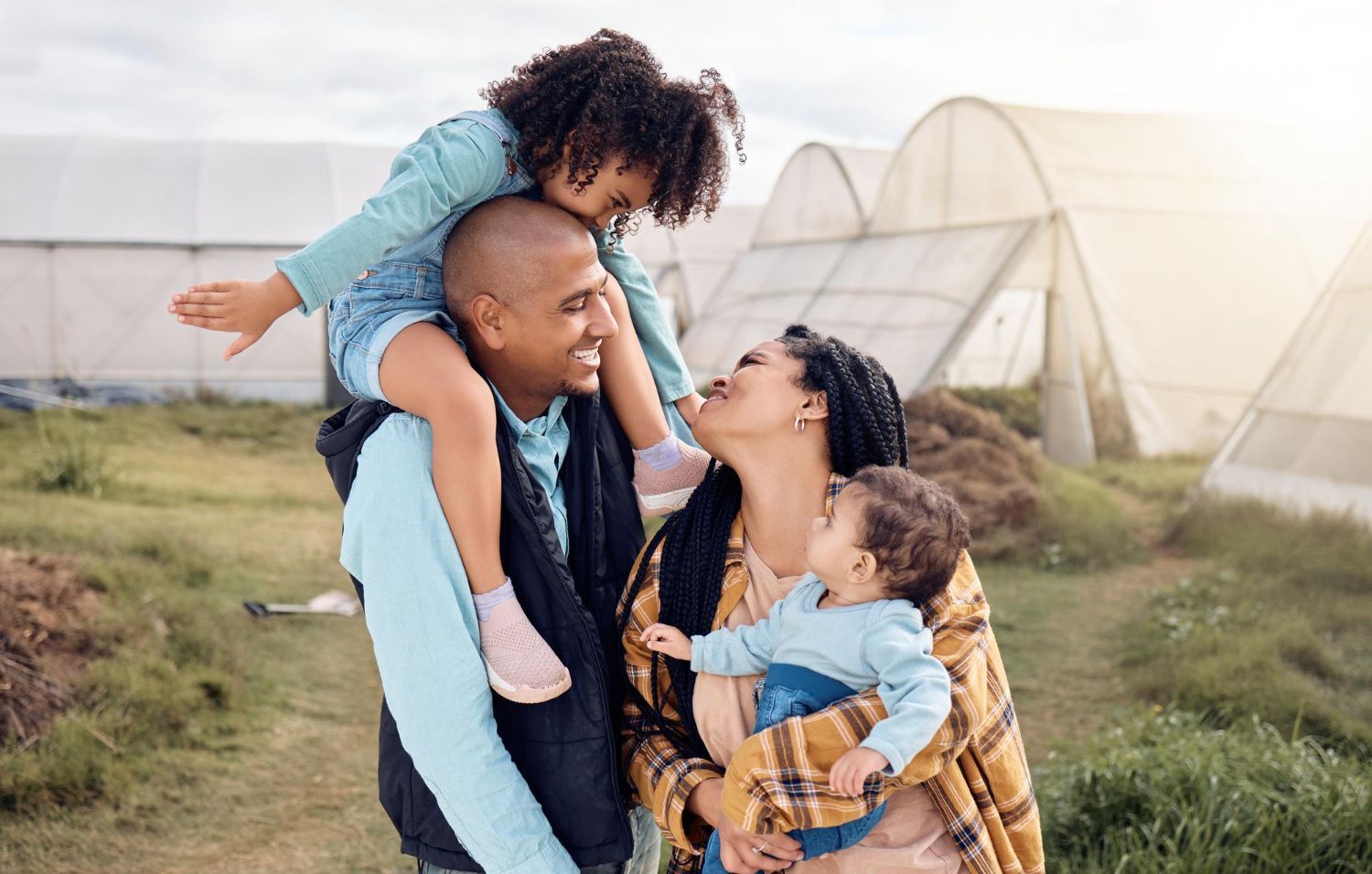 A man is carrying two children on his shoulders in a field. 