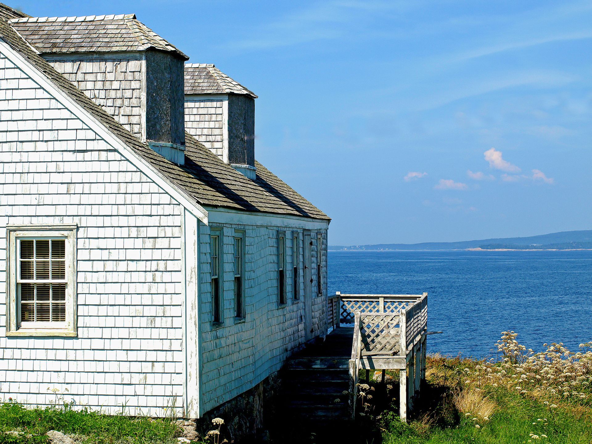 A white house with a deck overlooking the ocean 