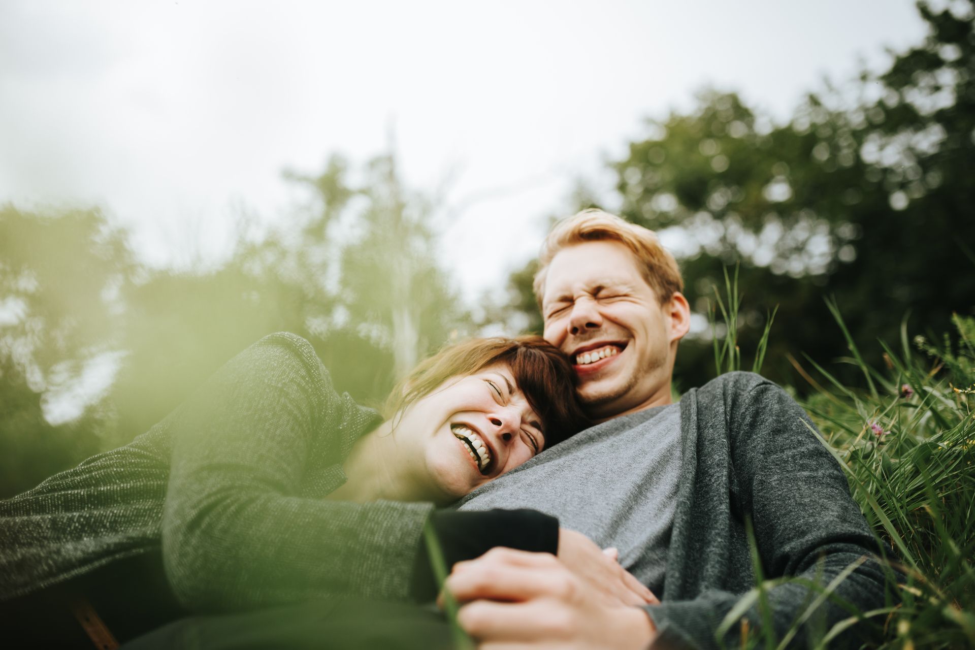 A man and a woman are laying in the grass and laughing. 