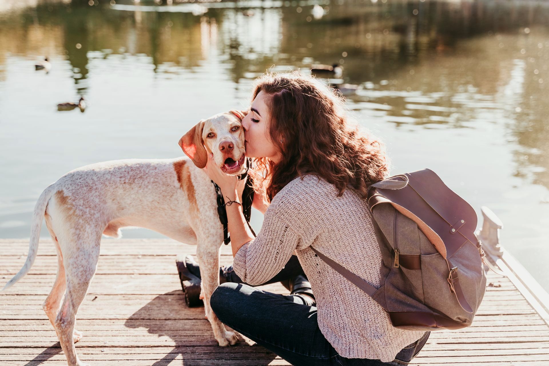A woman is kissing a dog on the nose on a dock. 
