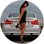 A woman in a black dress is standing in front of a white car.