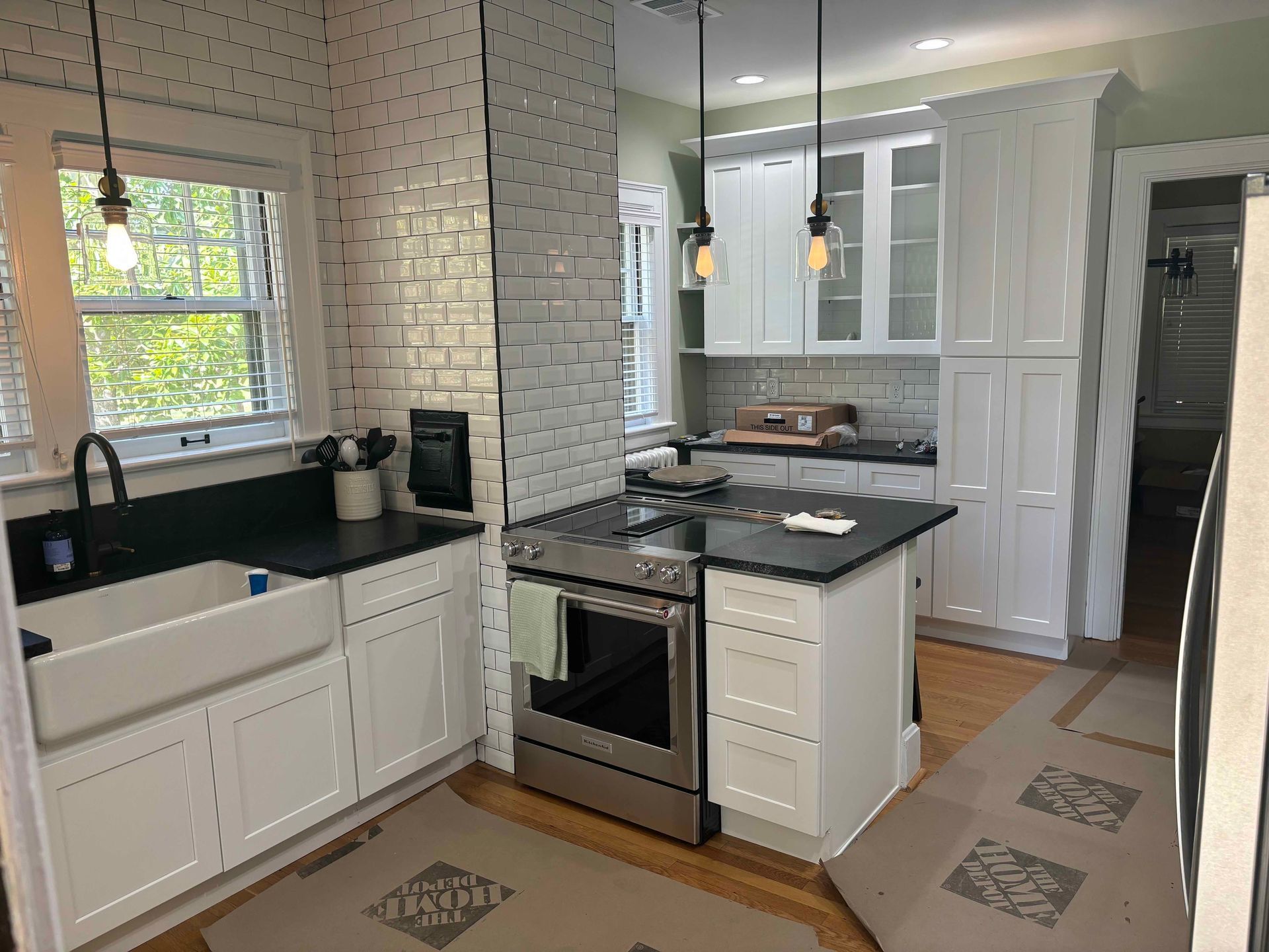 A bright, modern farmhouse kitchen featuring white cabinets, black countertops, a farmhouse sink, and a white brick wall.