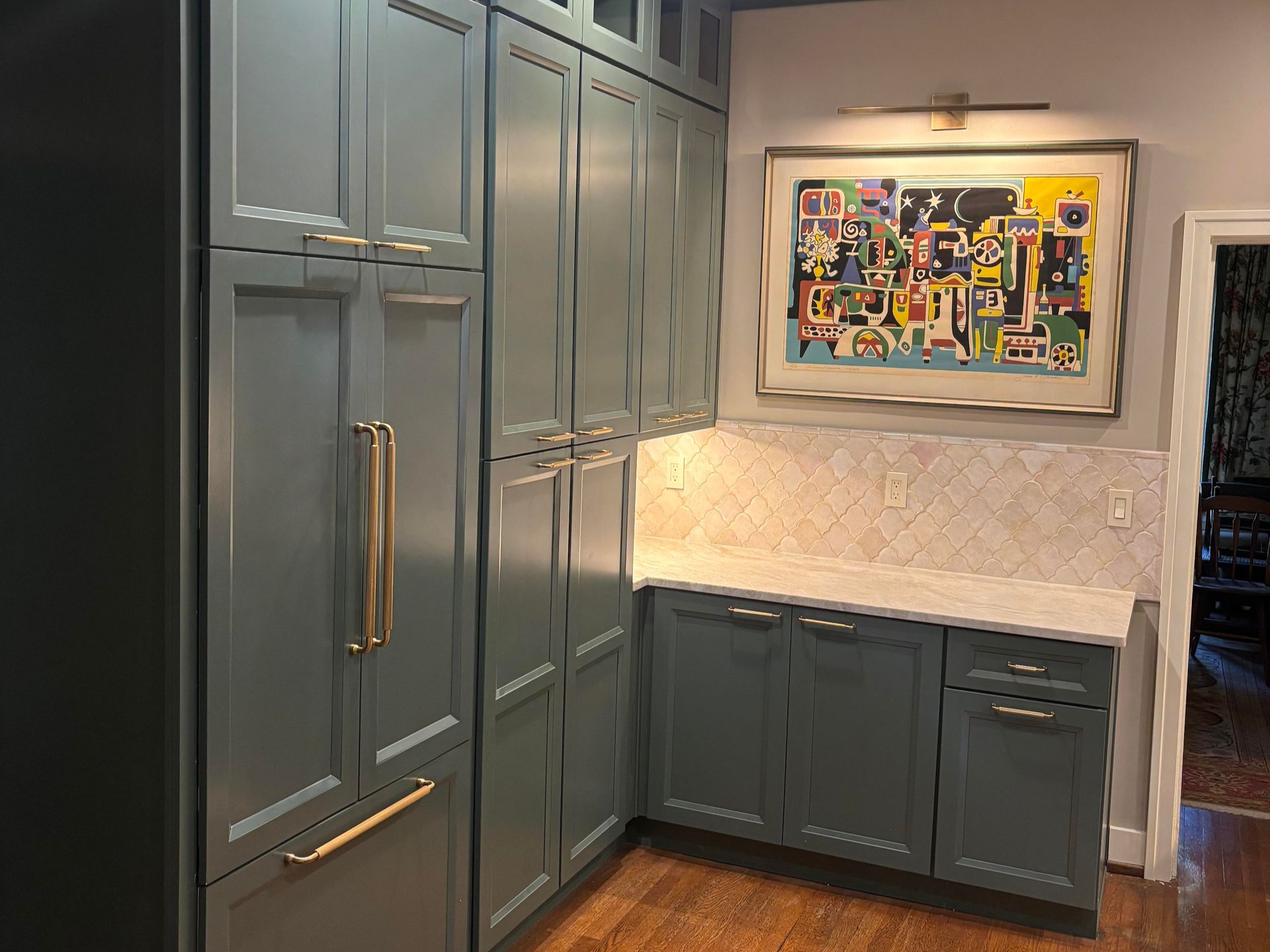 Blue kitchen cabinets with gold hardware, white countertop, artwork, and light fixture.
