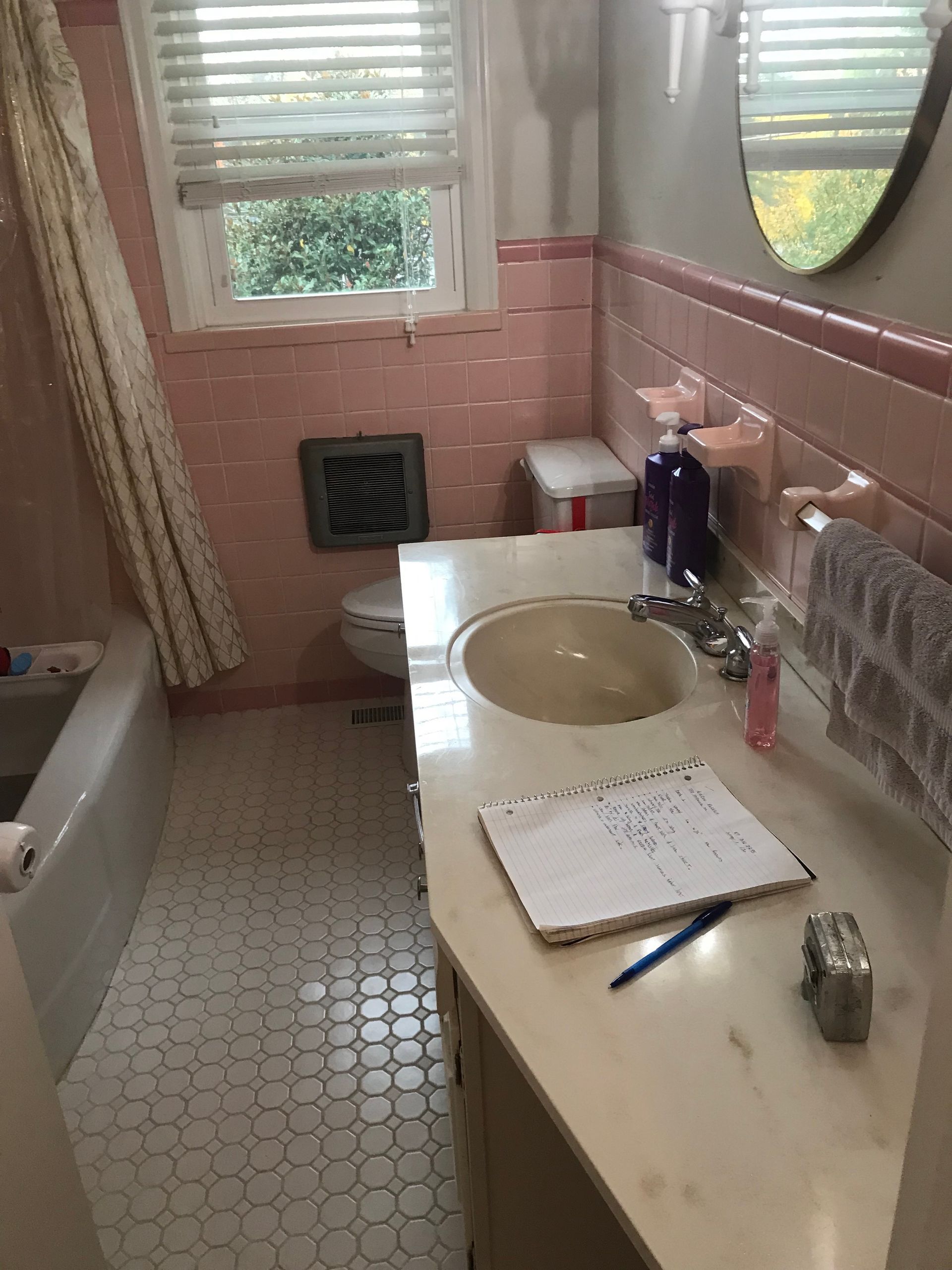 A bathroom with pink tiled walls, a white vanity with a sink, a bathtub with a curtain, and small white floor tiles.
