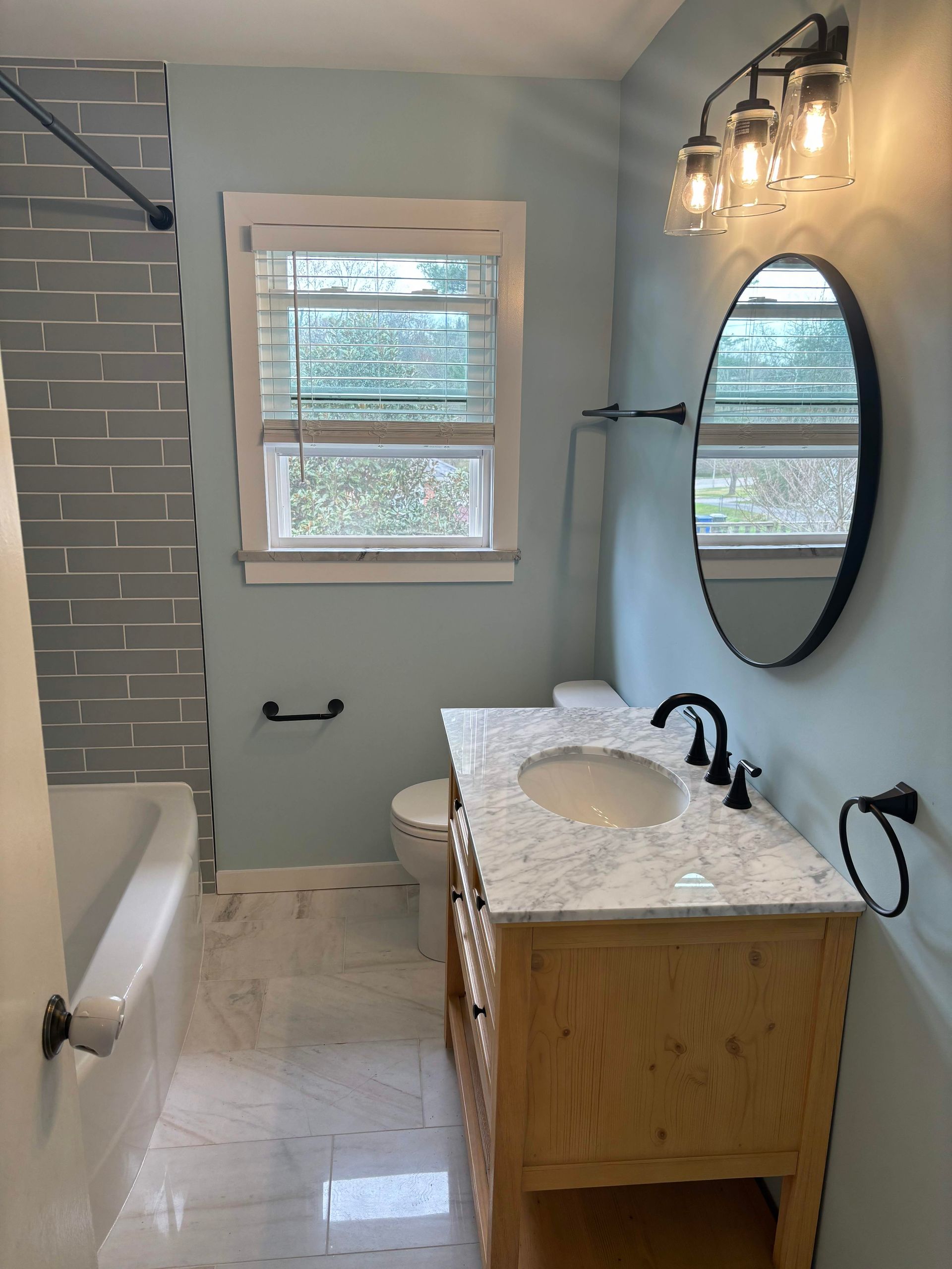 Bathroom with light blue walls, wood vanity, marble countertop, and gray tiled shower.