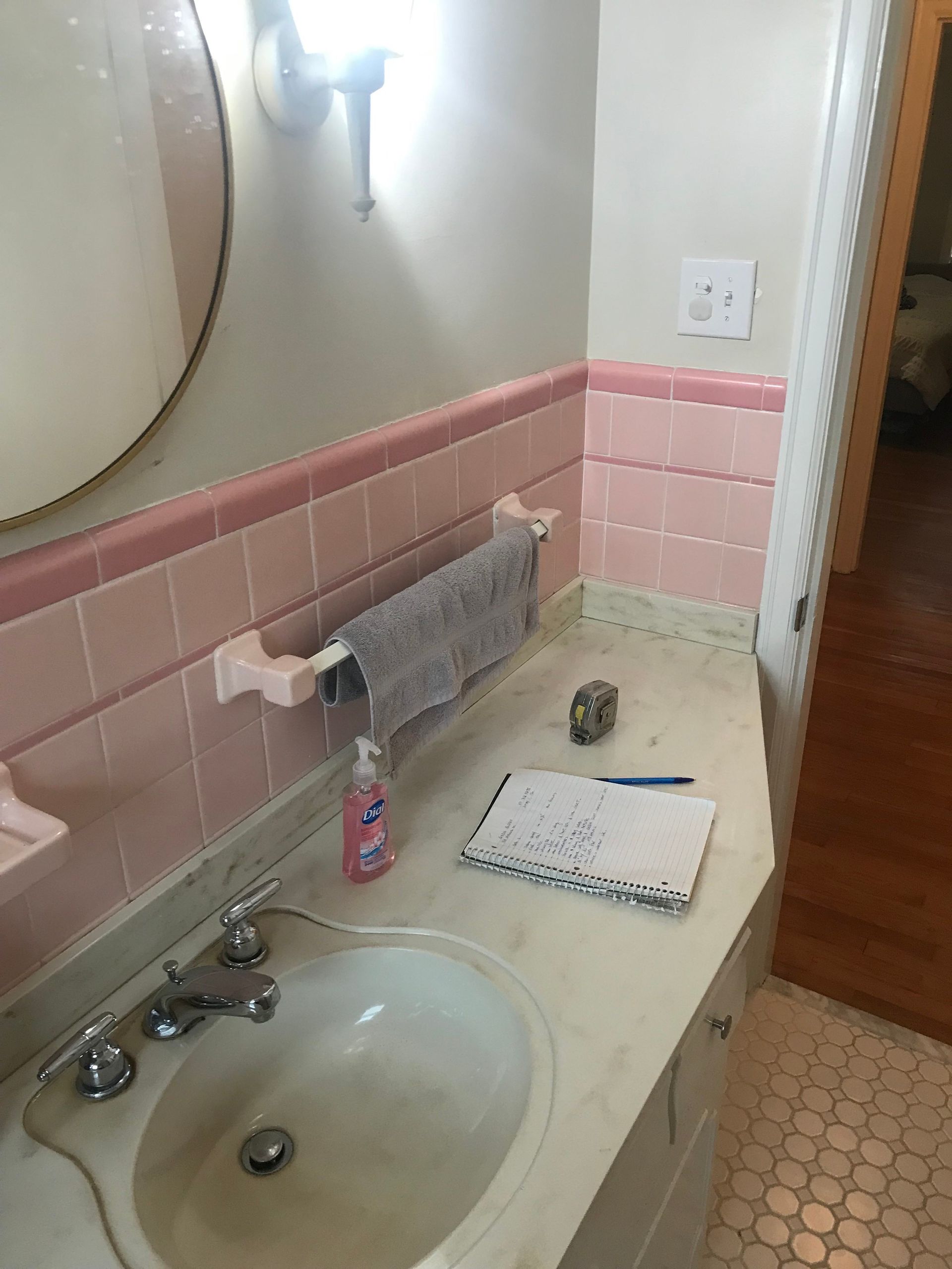 A bathroom vanity featuring a sink, pink tiled wall, a towel bar, and a notebook on the counter.