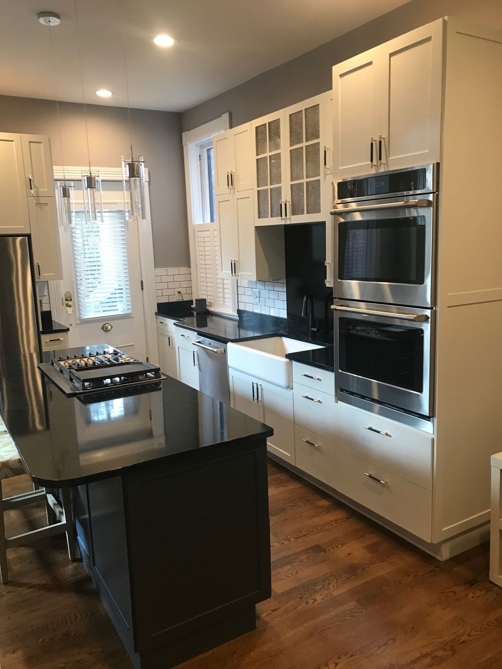 Modern white kitchen with black countertops, stainless steel appliances, and wood flooring.