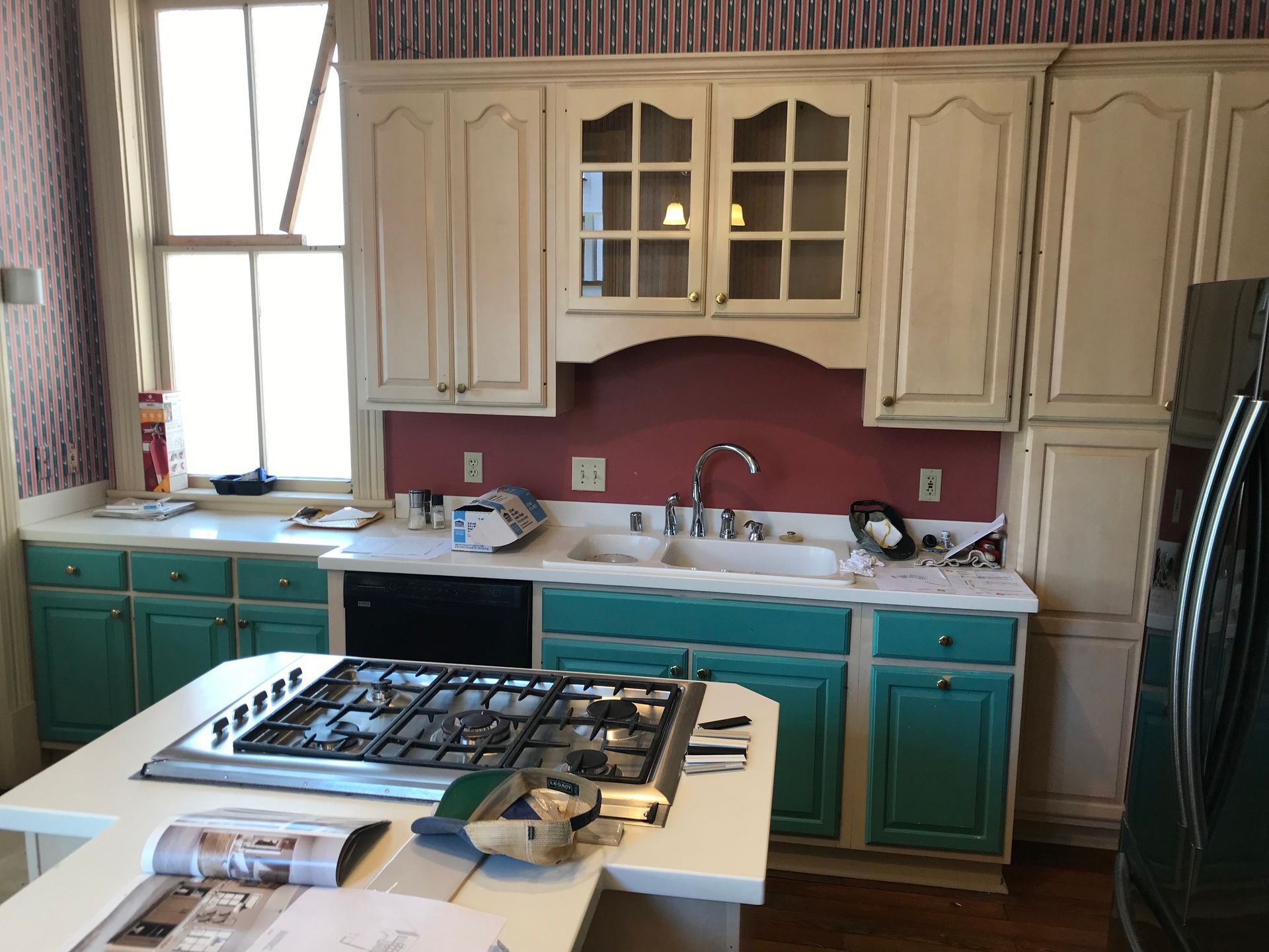 A kitchen with white upper cabinets, teal lower cabinets, a red backsplash, and a central island with a gas cooktop.